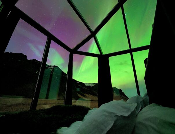 Glass igloo bedroom with king size bed, aurora lights up the sky