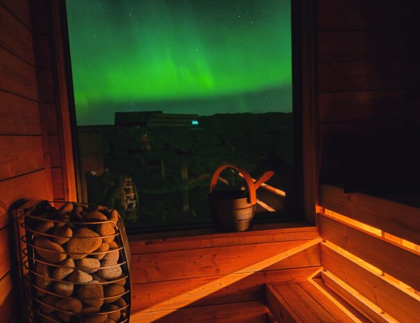 custom build Finnish sauna in wellness retreat Iceland, green waves of aurora seen outside the window