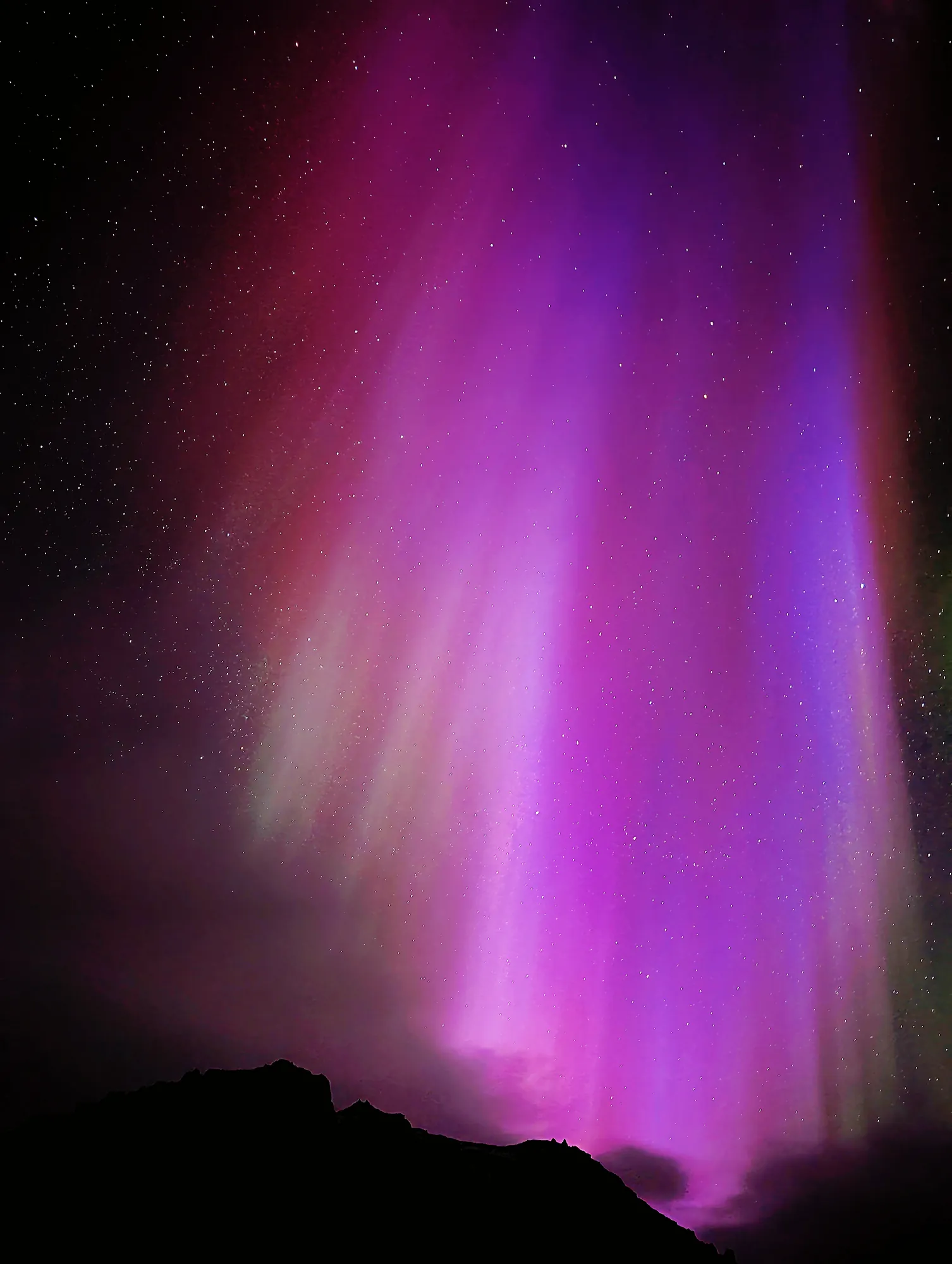 Purple and pink aurora corona directly overhead in a dark sky, South Iceland