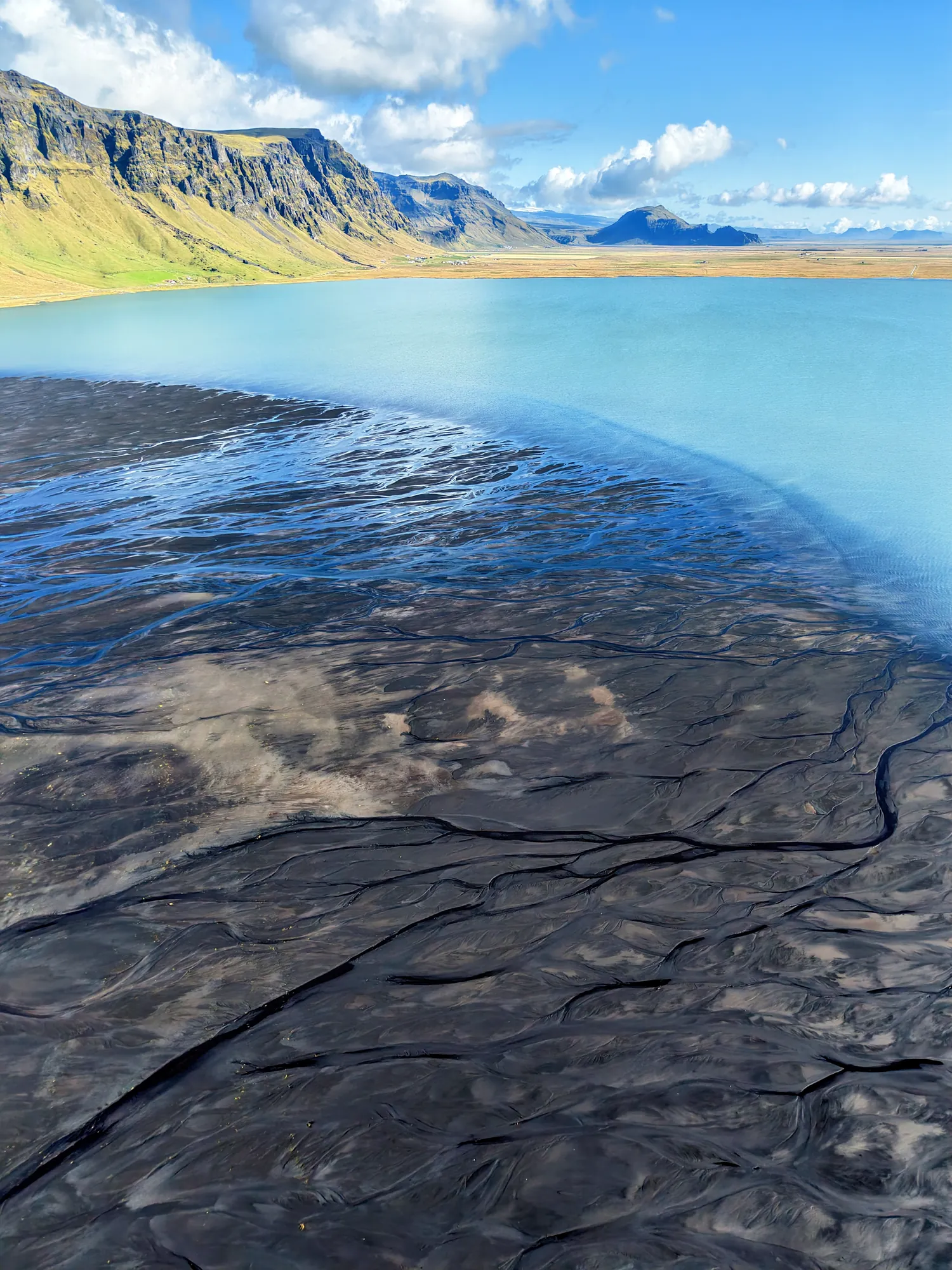 Turquoise water of Holtsós lagoon below the Eyjafjöll mountains on a summer day