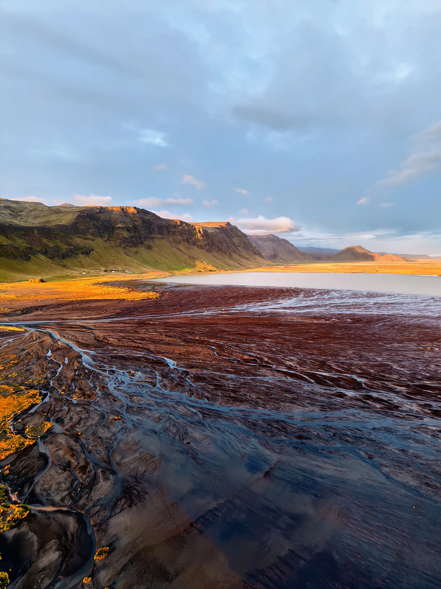 Aerial view of Holtsós lagoon near Ormskot under Eyjafjöll, with dark sand channels and evening light