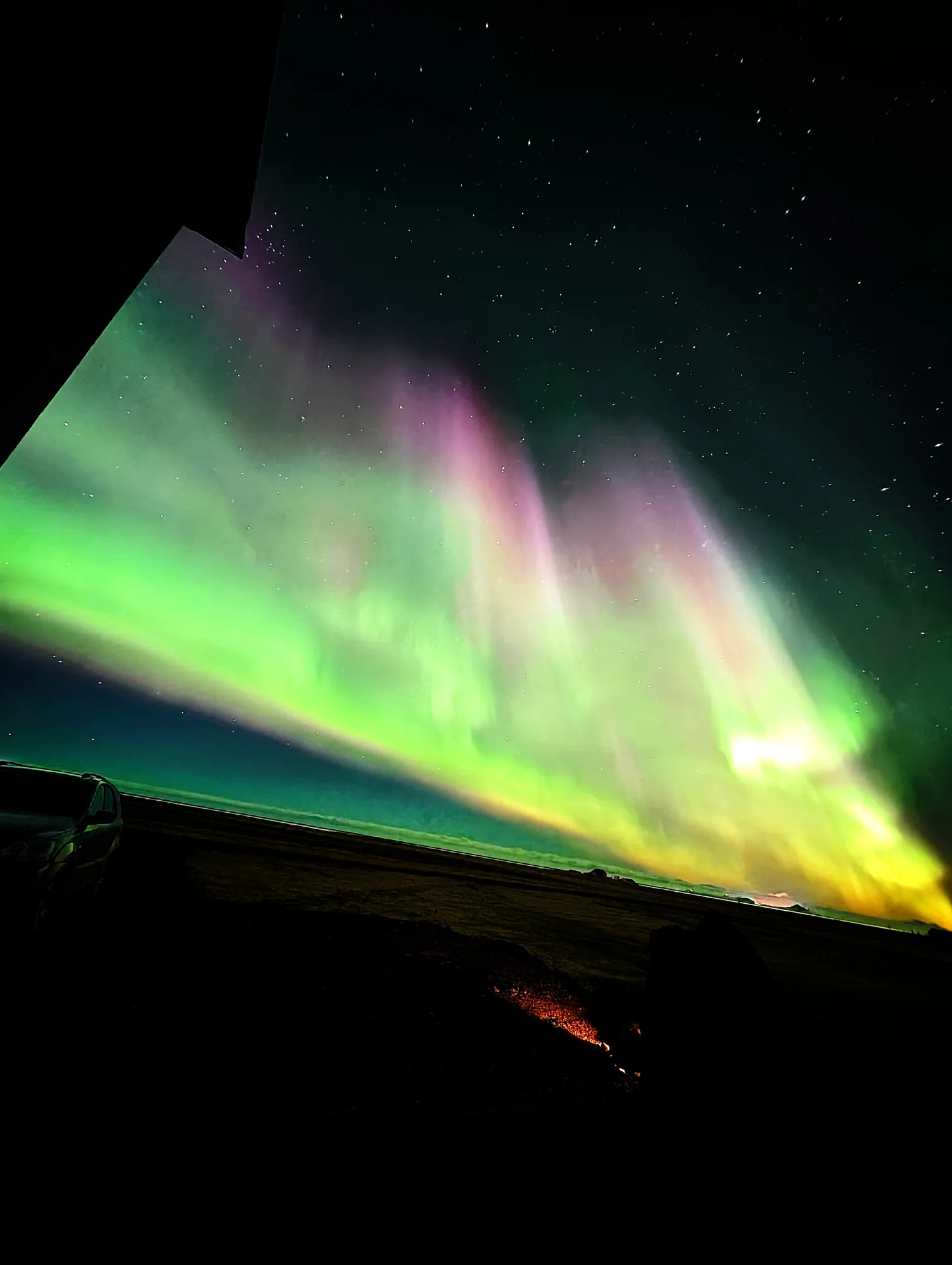 Green and pink aurora seen from beside one of the cabins at Ormskot, looking out over the flat South Iceland lowland