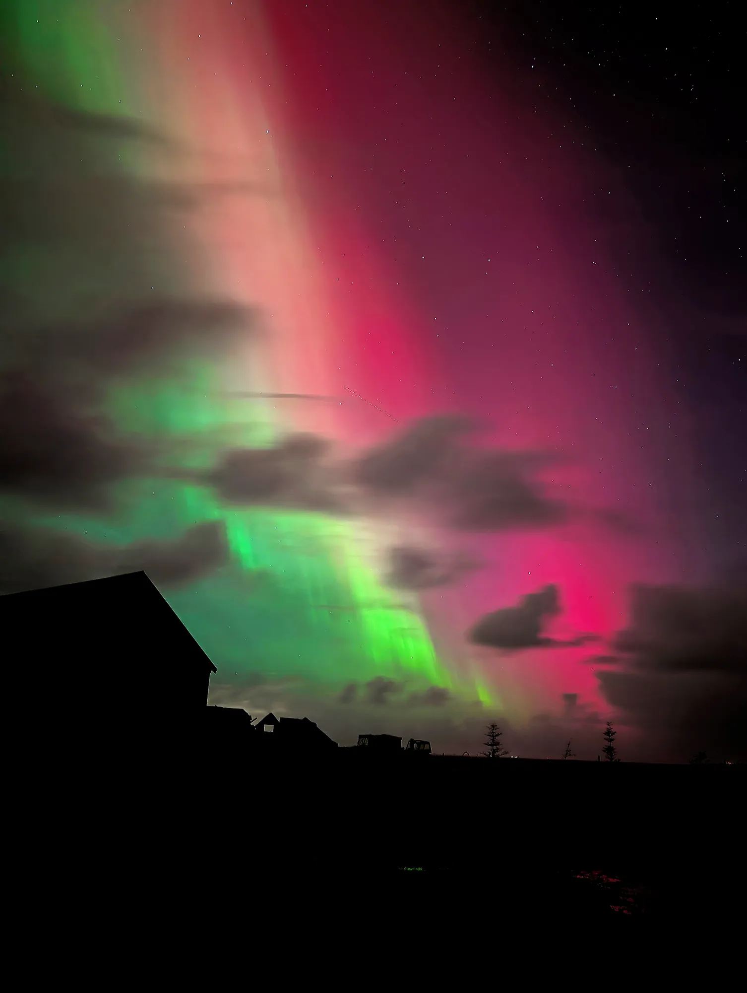 Pink and green northern lights over the Ormskot farm buildings in silhouette