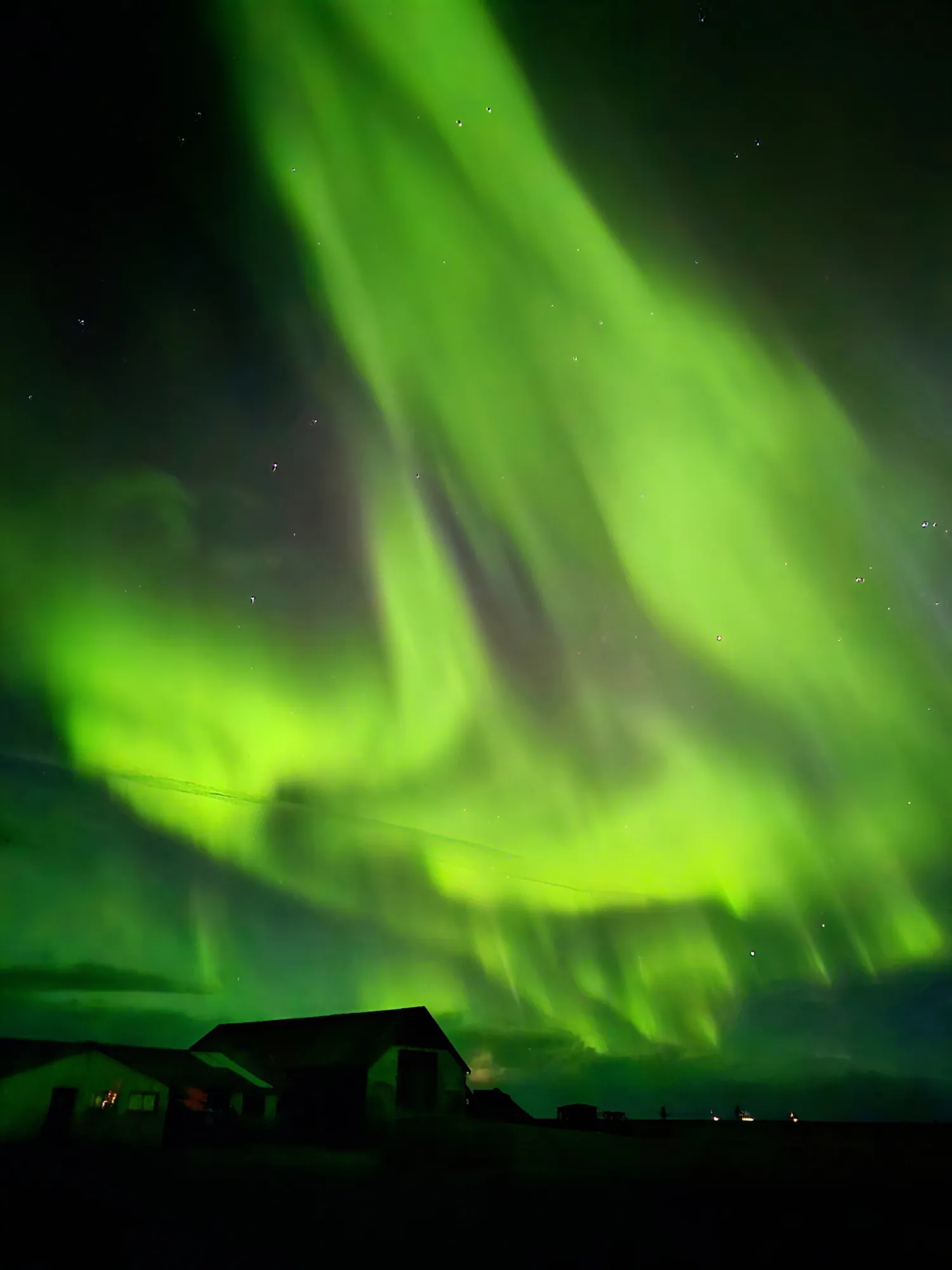 Bright green aurora curtains above the farm buildings at Ormskot, South Iceland
