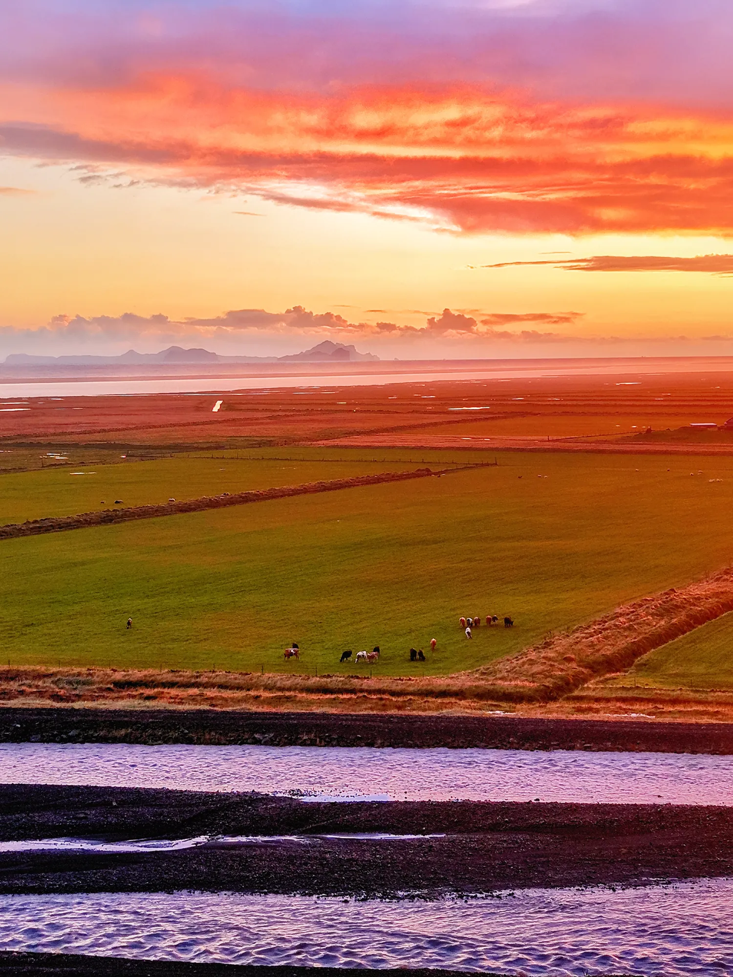 Drone view from Ormskot farm at sunset over green fields and a river, with the Westman Islands on the horizon