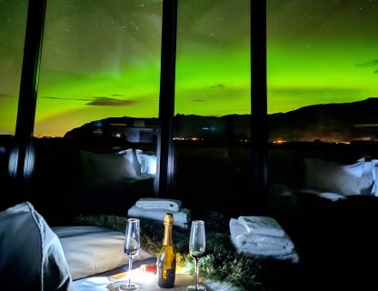 Romantic getaway in the arctic with champagne on bed and aurora dancing outside, Iceland