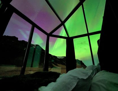 Glass igloo bedroom with king size bed, aurora lights up the sky