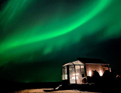 Aurora lights up the sky over glass igloo Iceland